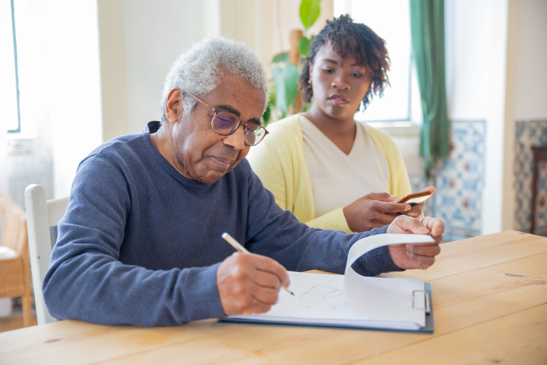 A support worker and an older person going through a care plan and its records at a table